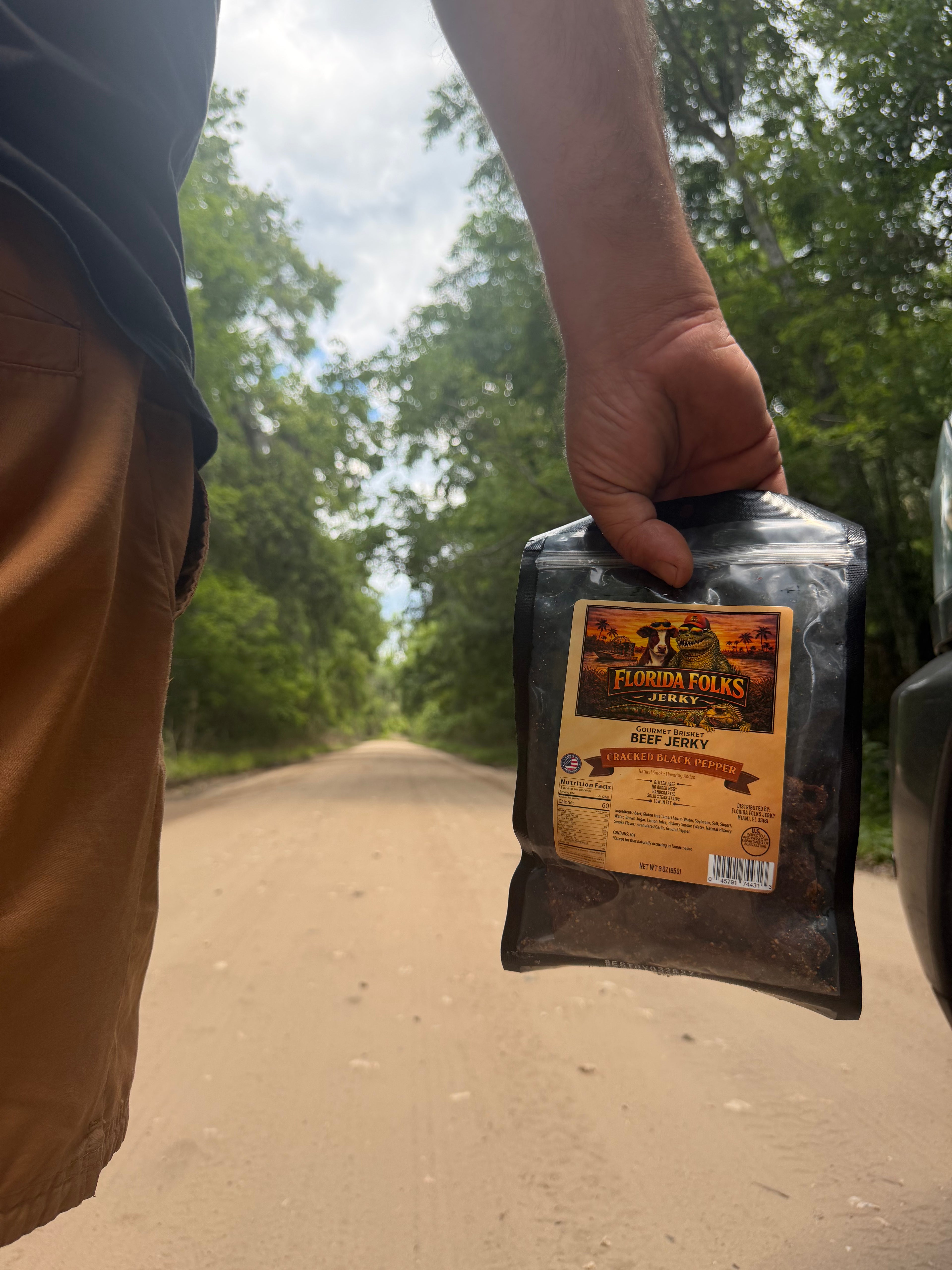 Person holding a package labeled 'Florida Folks' on a dirt road with trees in the background